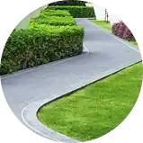 A winding paved walkway curves through a neatly manicured lawn in Lewisberry, bordered by trimmed green hedges and small shrubs, leading towards a building in the background.